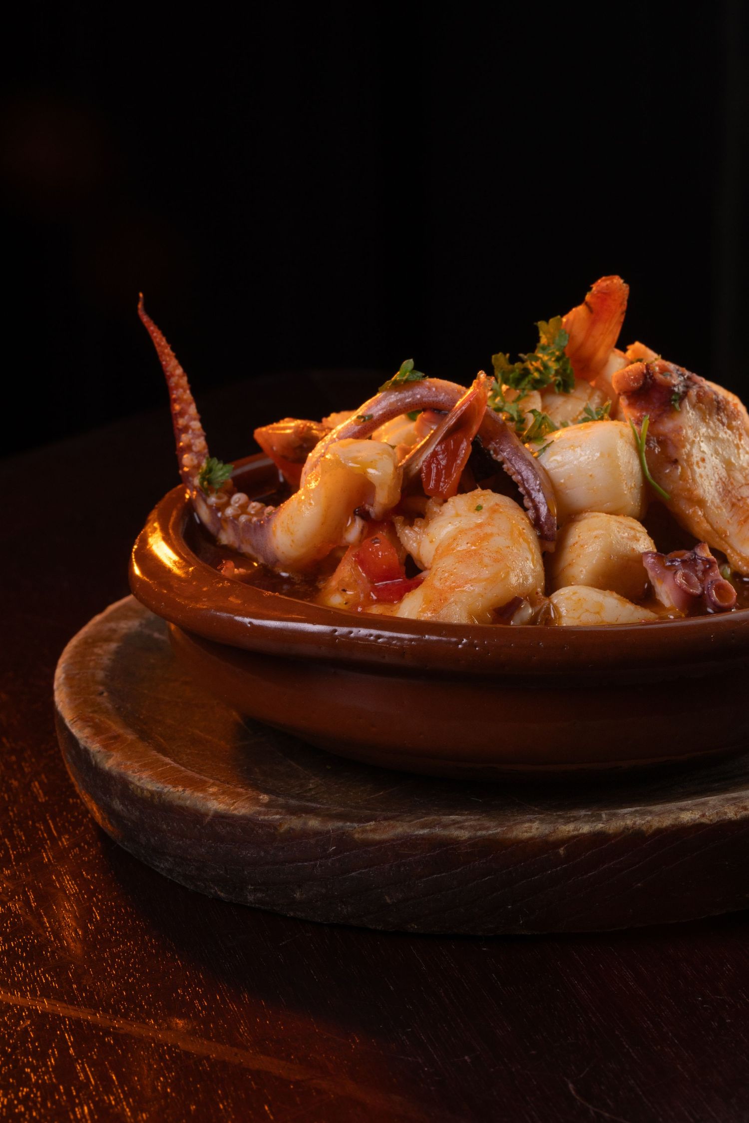 Fresh seafood dish with octopus tentacles and shrimp served in a rustic clay bowl on dark wooden surface.