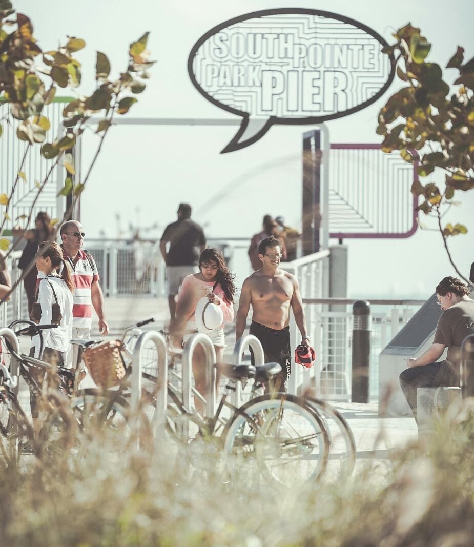 Group of cyclists gathered near a pier sign on a sunny day.
