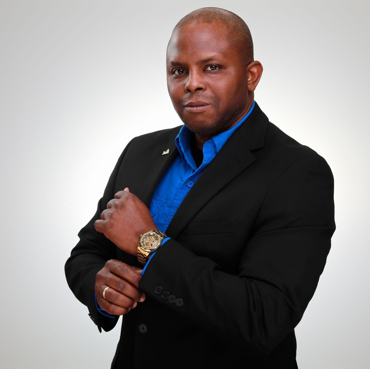 Professional in black suit and royal blue shirt poses confidently with gold watch.