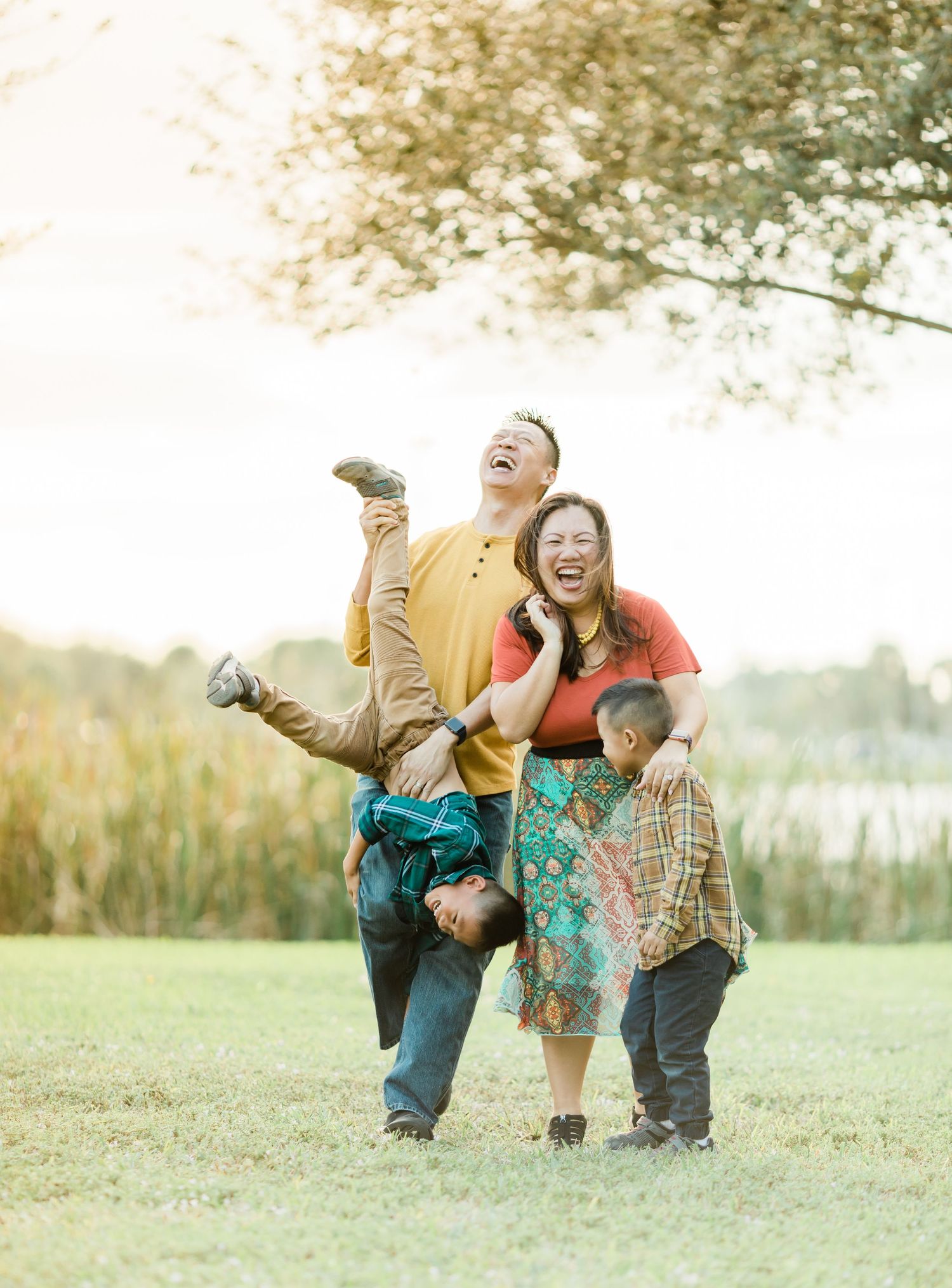 A joyful family plays and laughs together in a grassy field at sunset.
