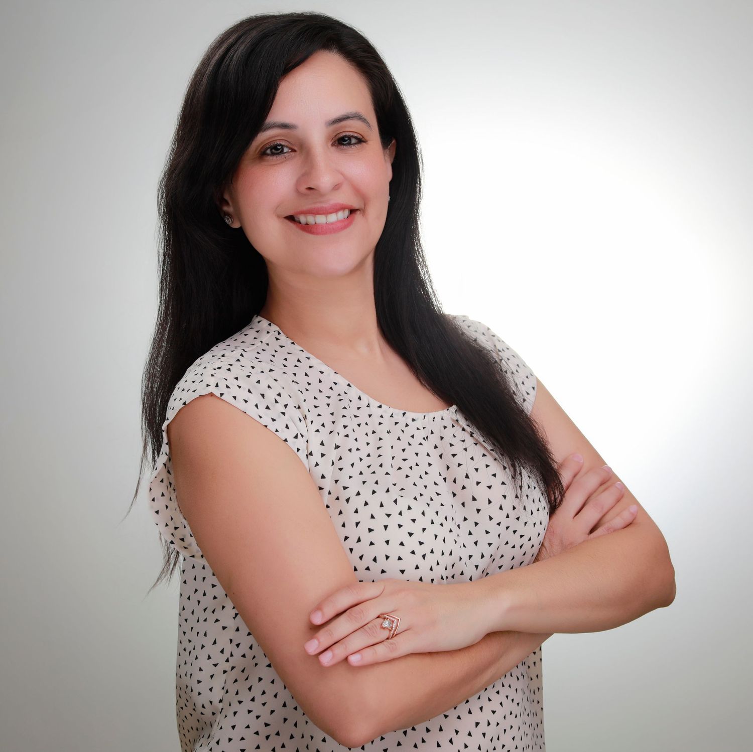Professional headshot wearing white patterned top with crossed arms against gray backdrop.