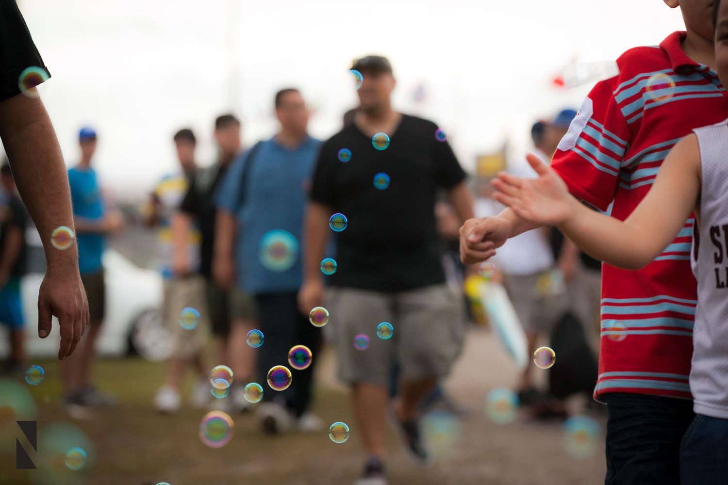 Colorful soap bubbles float through air at an outdoor gathering with people standing in casual dress.