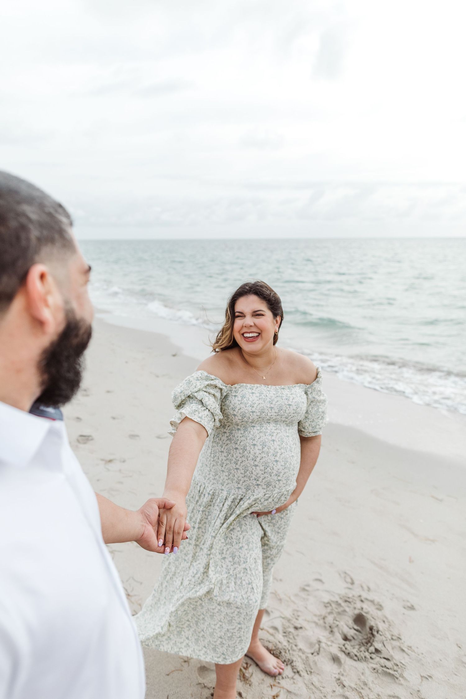 Couple enjoying a romantic moment on a cloudy beach, with waves and sand in the background.