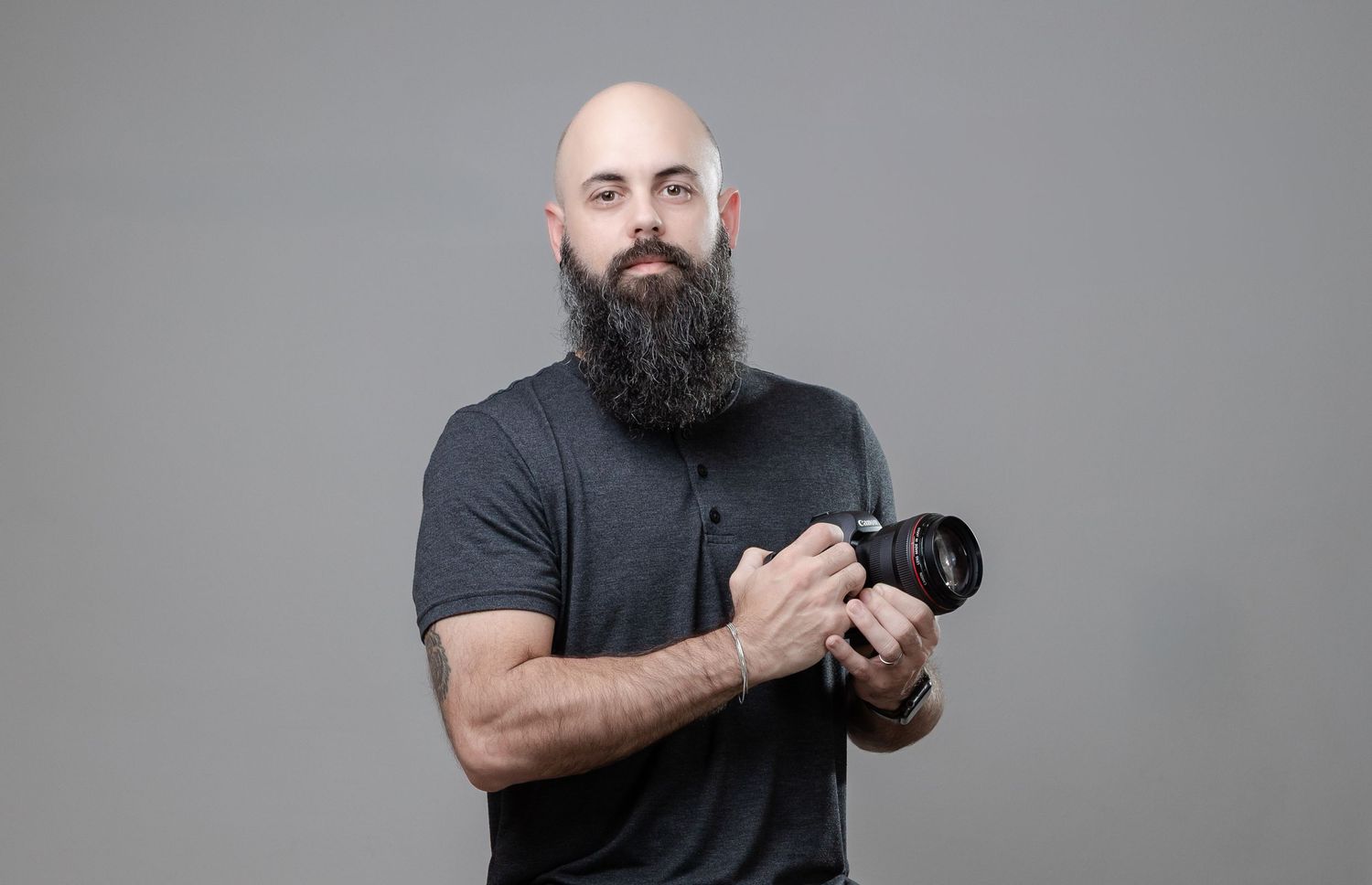 Professional photographer in black t-shirt holding camera against gray background.