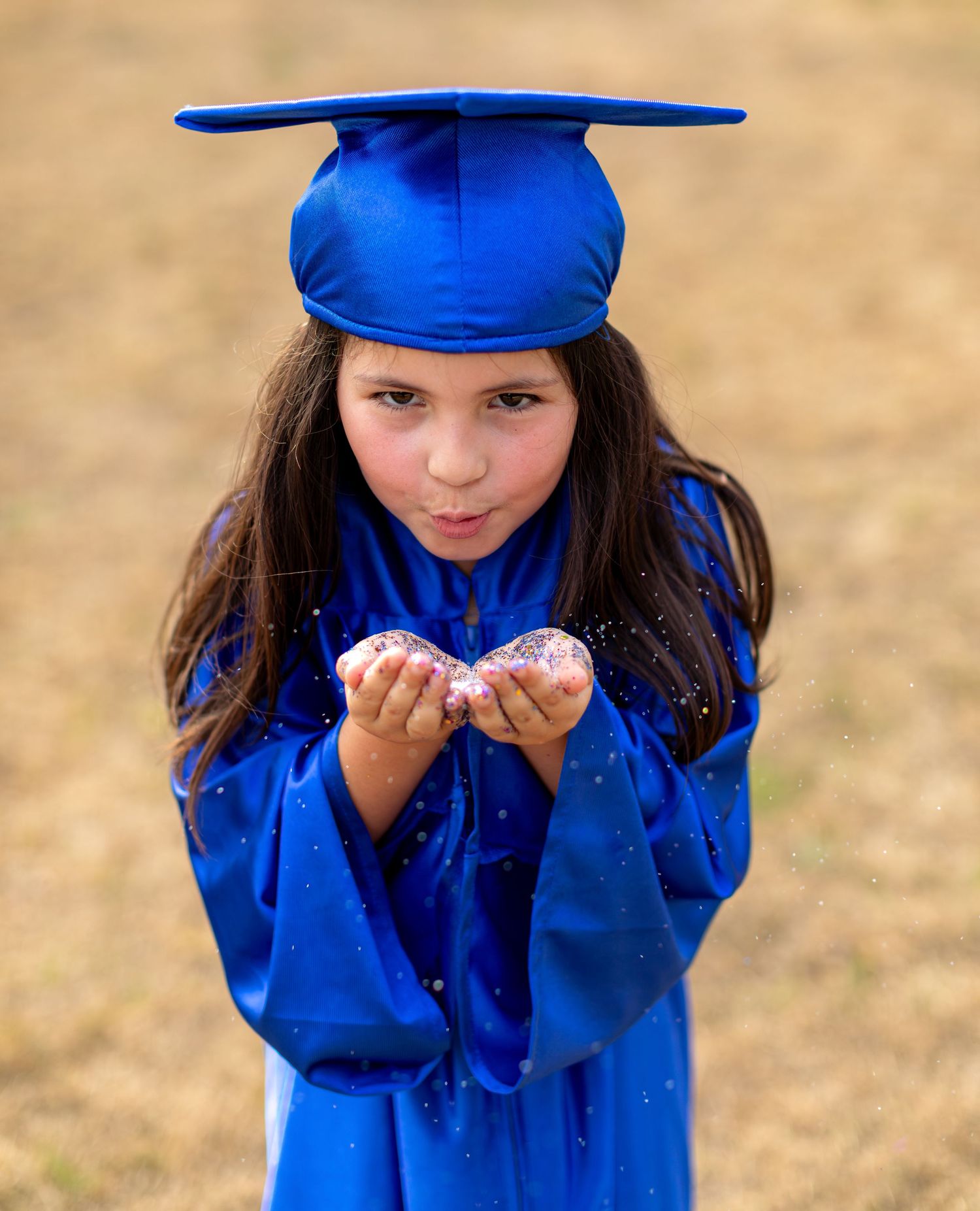 Young graduate in bright blue cap and gown blows a playful kiss during outdoor graduation photo shoot.