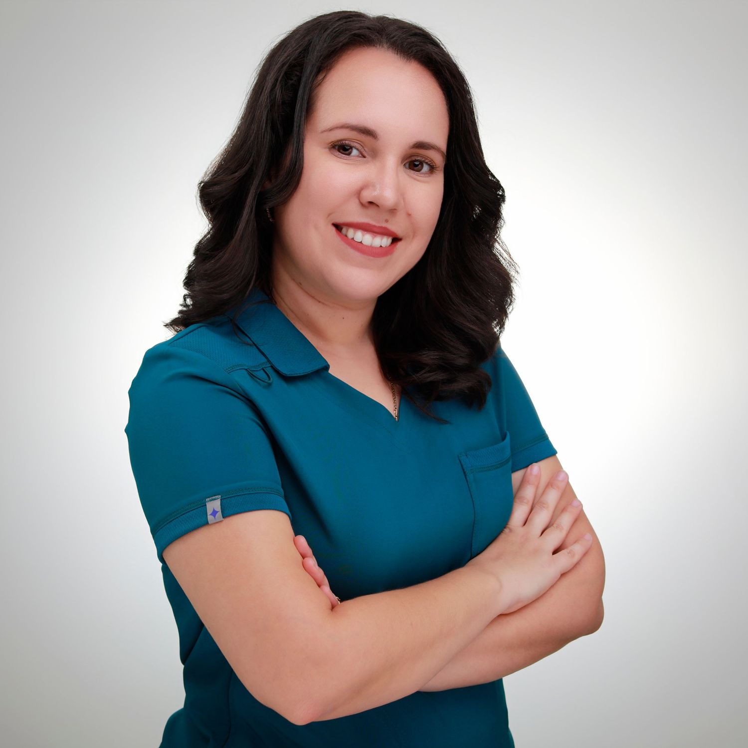 Professional studio portrait in teal polo shirt with arms crossed.