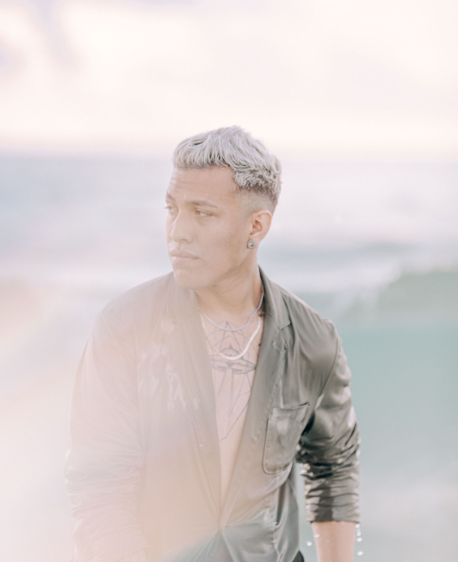 Portrait of someone in olive jacket against blurred ocean backdrop during golden hour.