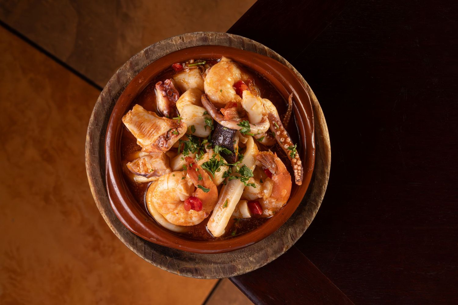 A bowl of seafood stew with shrimp and mushrooms in a rich broth garnished with fresh herbs.
