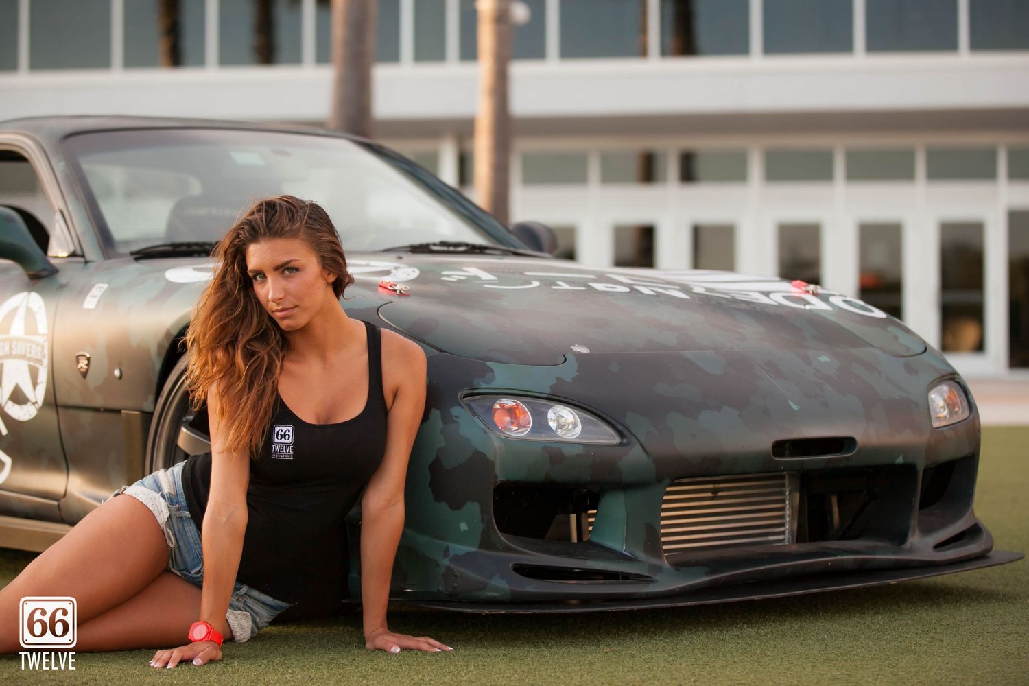 Modified black Mazda RX-7 with custom body kit parked in front of a modern building.