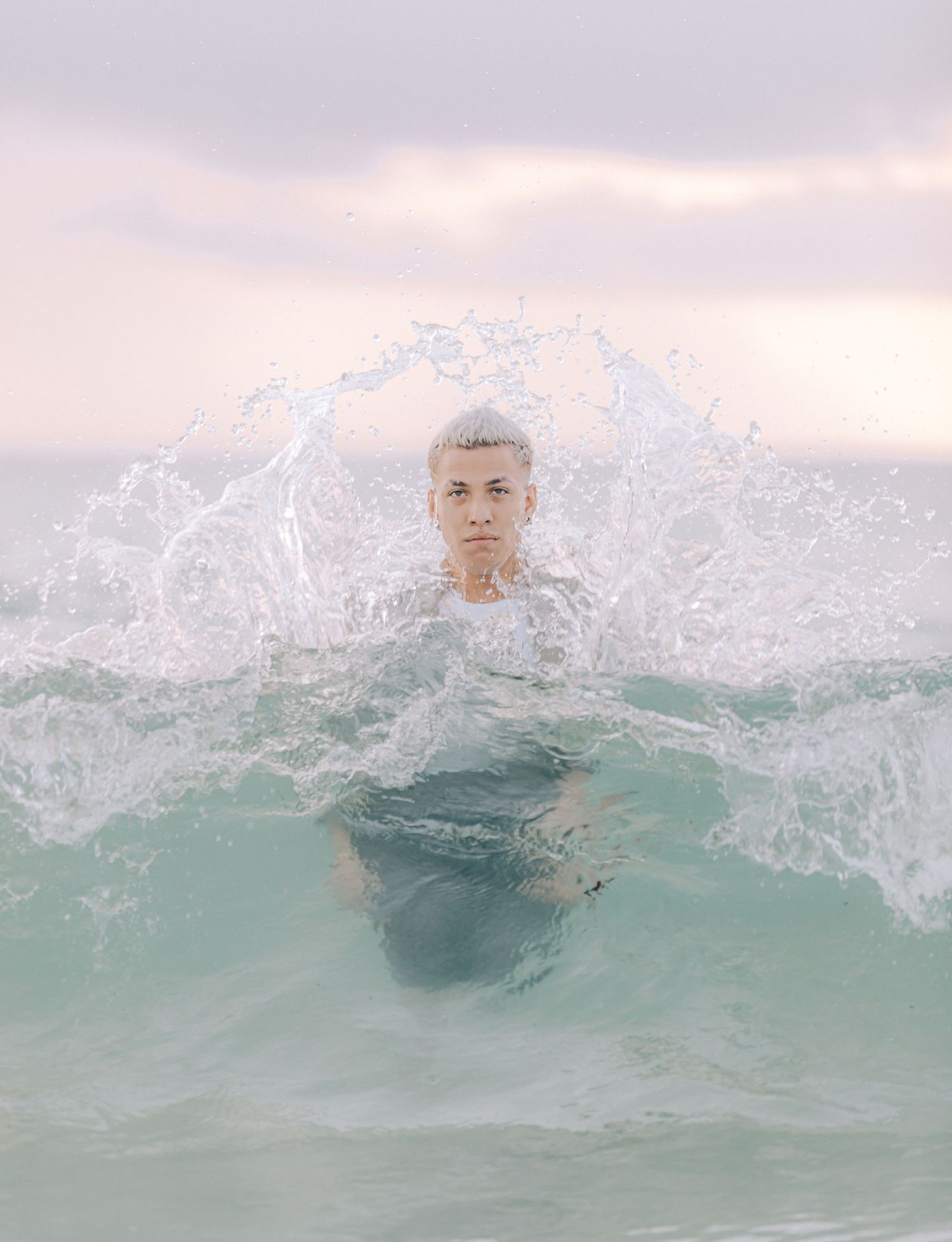 Person emerging from splashing turquoise ocean waves during sunset creating dramatic water spray effect.