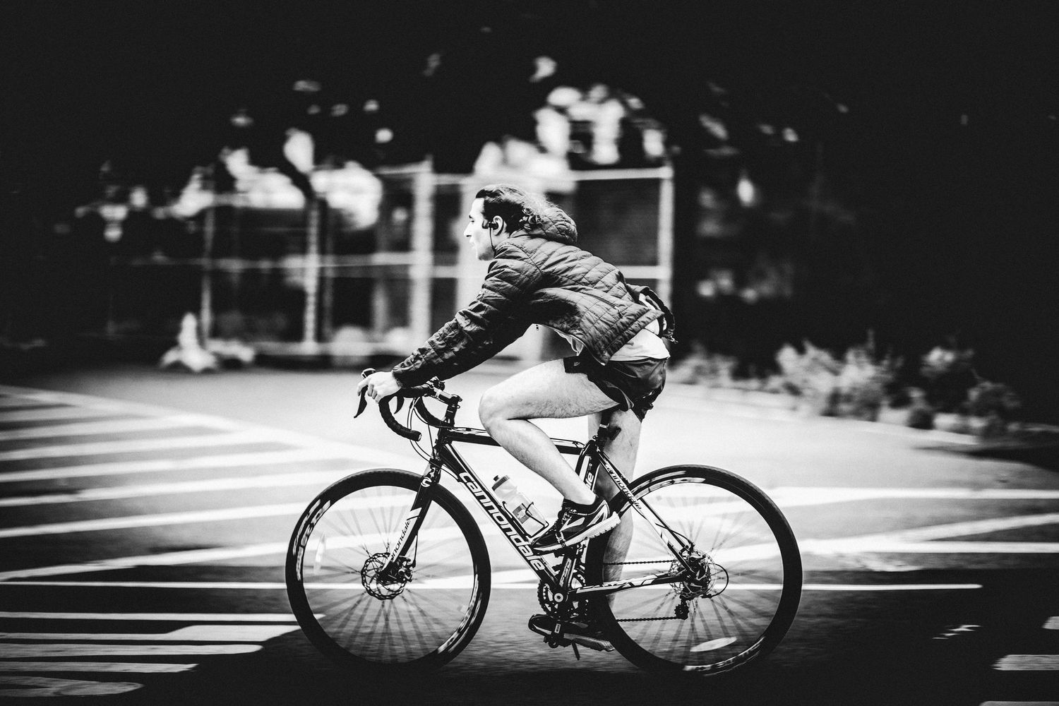 Black and white image of a cyclist riding through a city intersection.