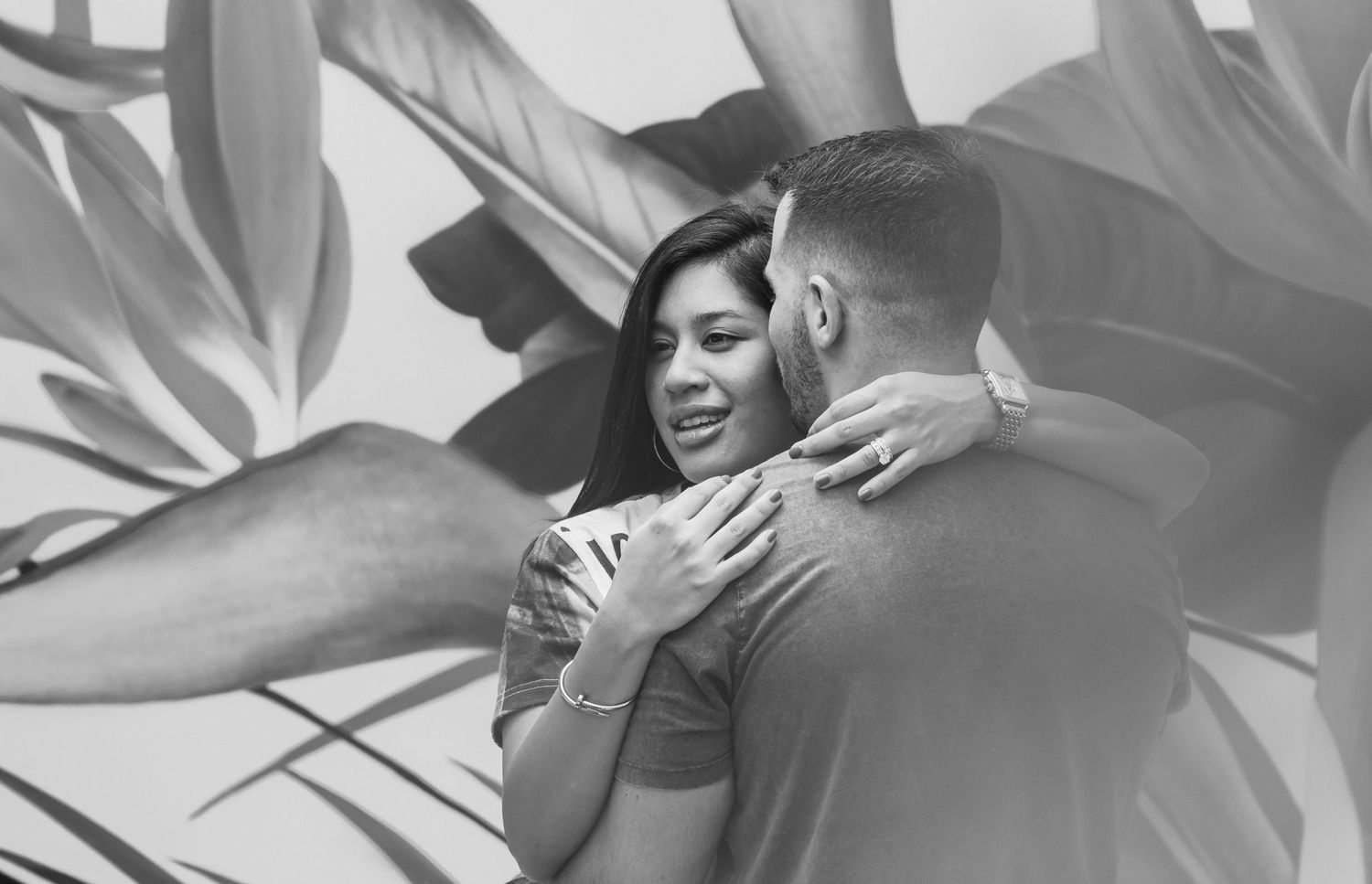 Intimate black and white portrait of couple embracing near tropical leaves.