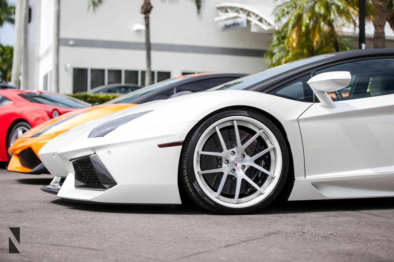 A white Lamborghini Aventador showcasing its aggressive front end design and custom wheels at a dealership.