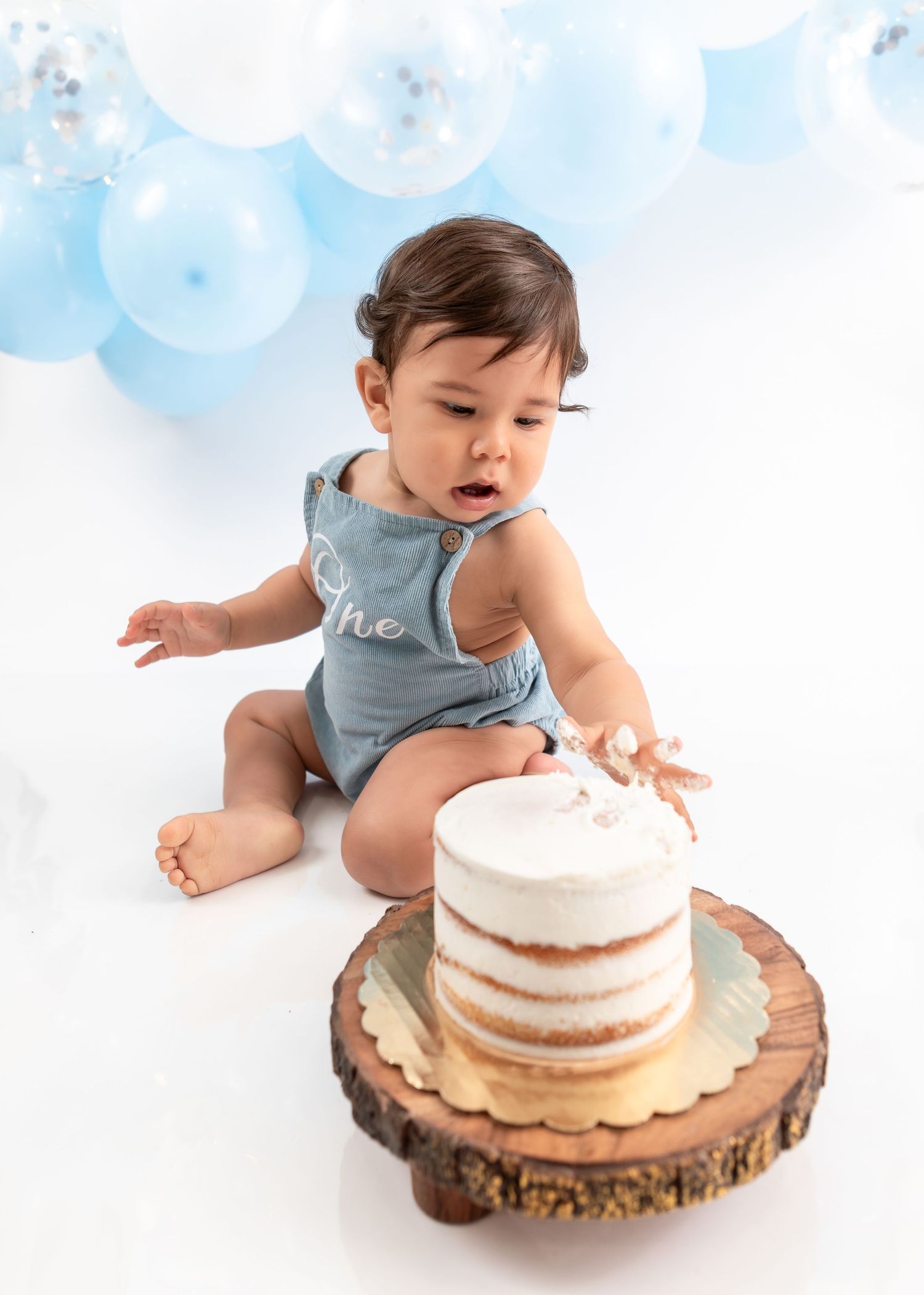 Baby reaching towards naked cake displayed on rustic wood cake stand.