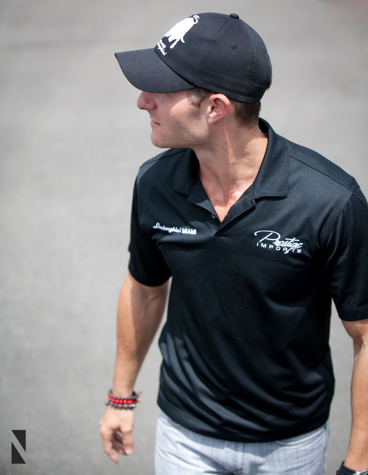 Someone in a navy baseball cap and black polo shirt with white logo at an outdoor event.