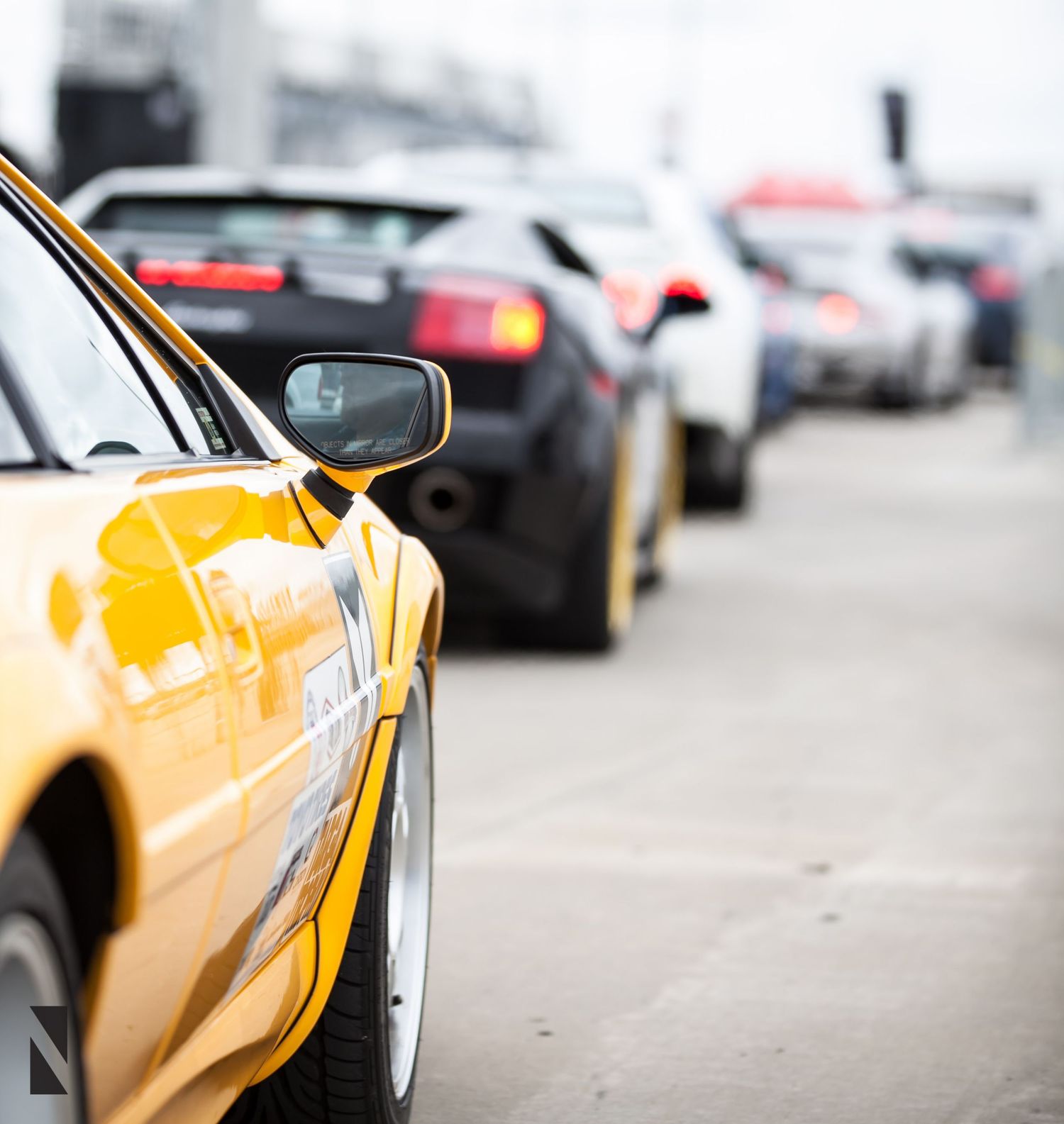 Yellow sports car in focus with a line of performance vehicles blurred in the background.