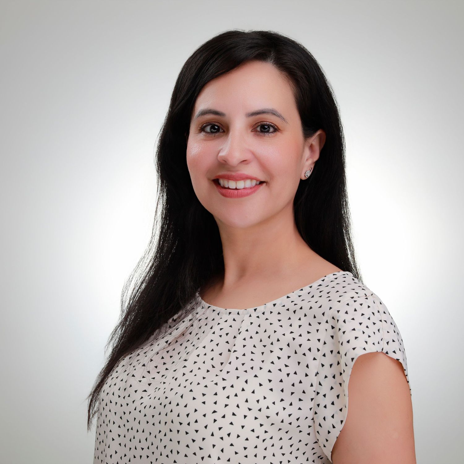 Woman in a dotted blouse smiling warmly against a light background in a professional headshot.