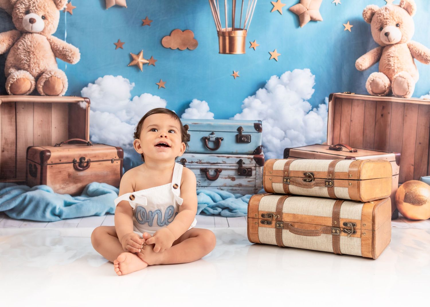 Baby sitting on floor with vintage travel theme backdrop with teddy bears and clouds.