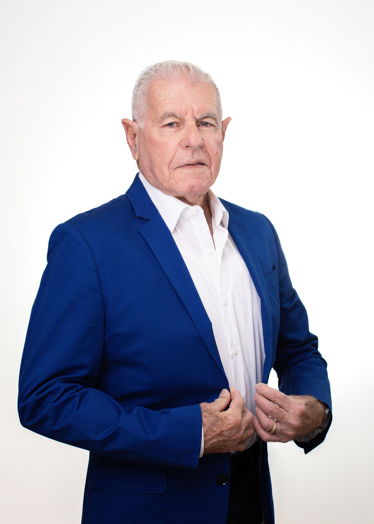 Professional portrait of senior man in bright blue suit jacket against white backdrop.