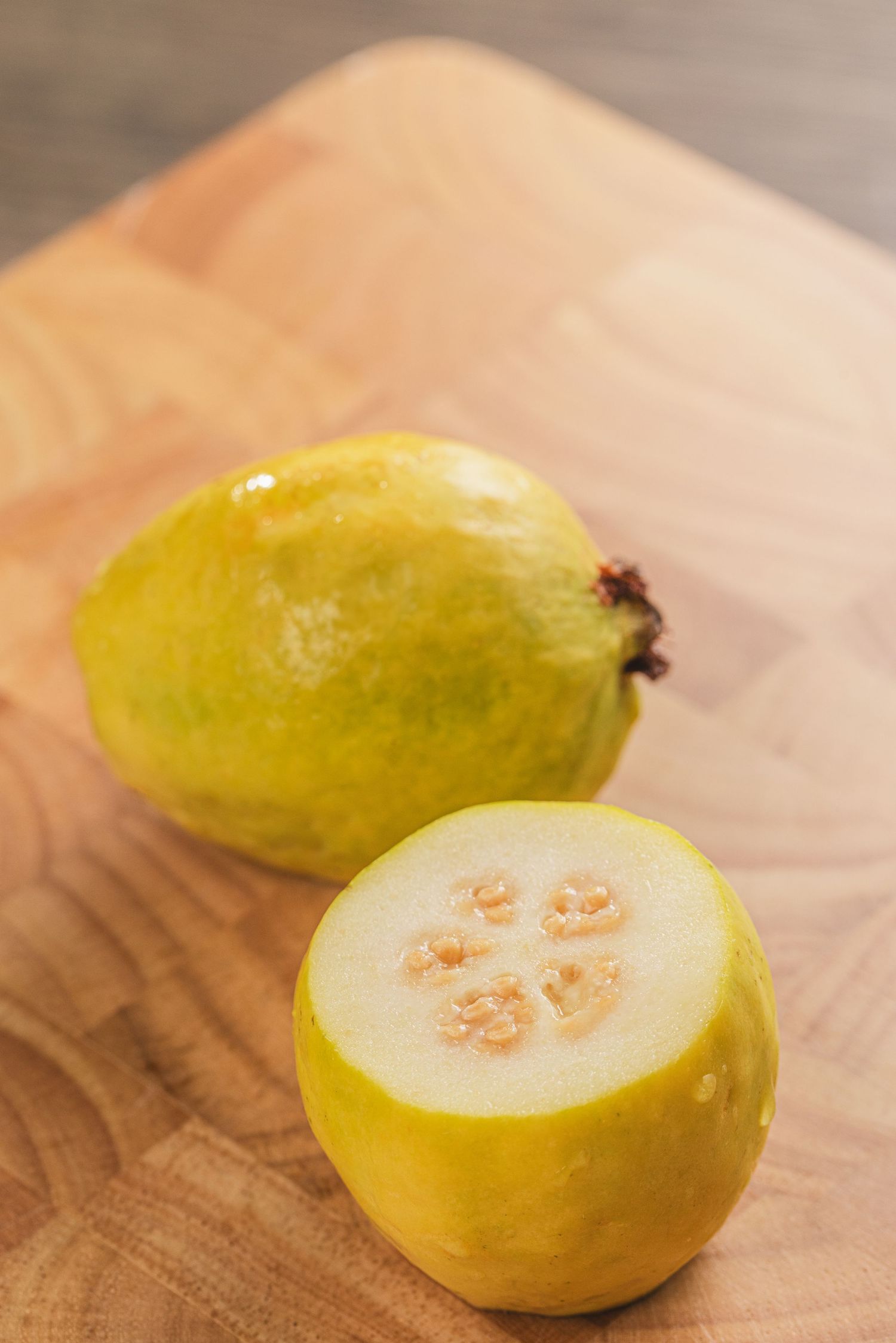 Fresh lemon cucumber sliced in half on a wooden cutting board showing its unique pale flesh and seeds inside.