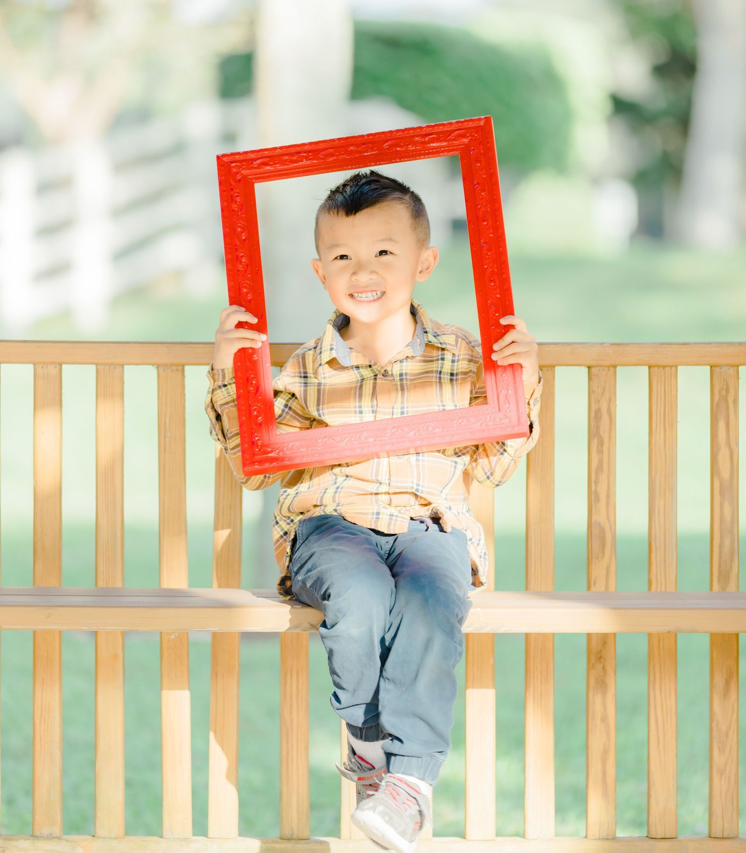 Child sitting on wooden bench holding red picture frame with joyful expression.