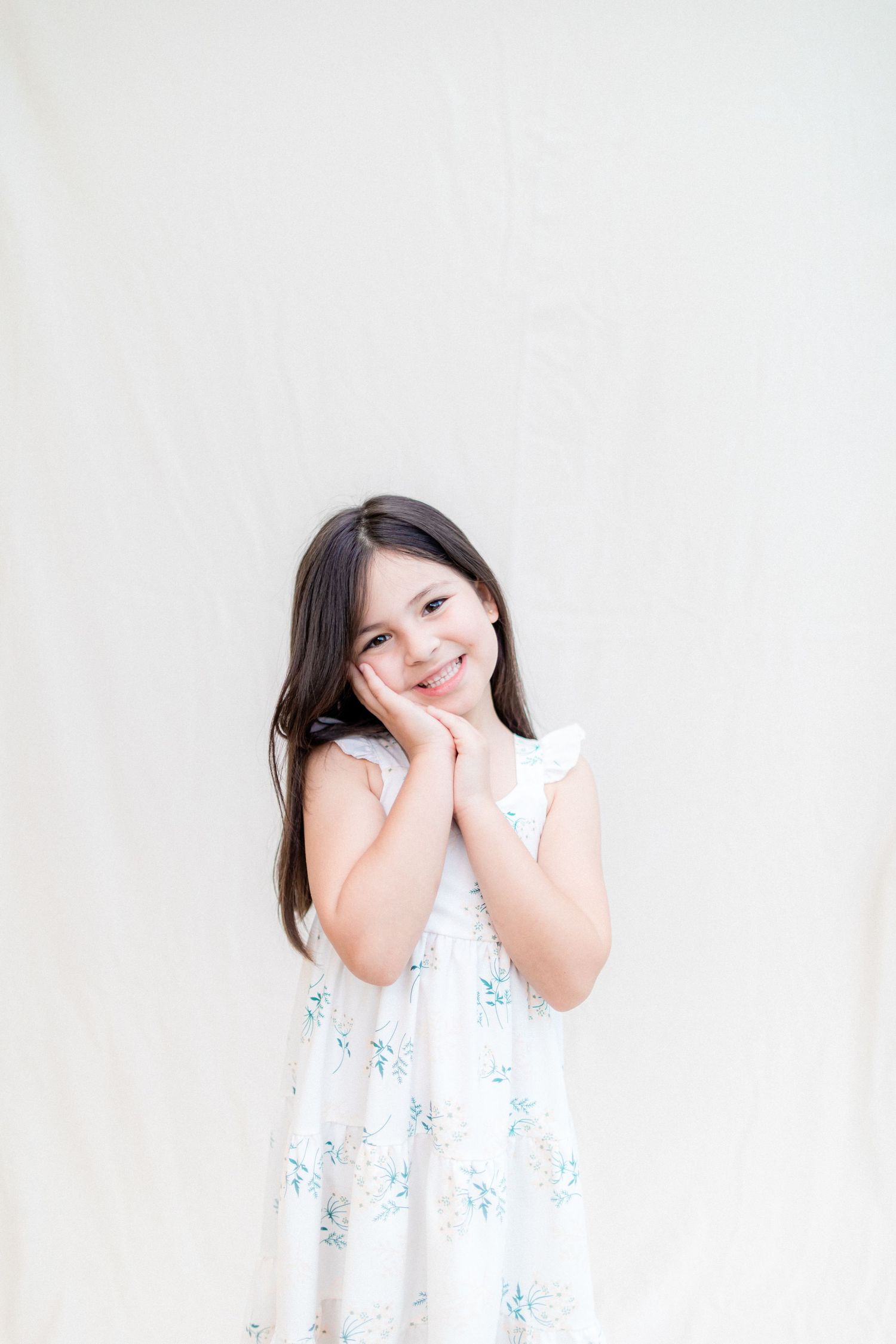 Sweet pose in white floral dress against light background.