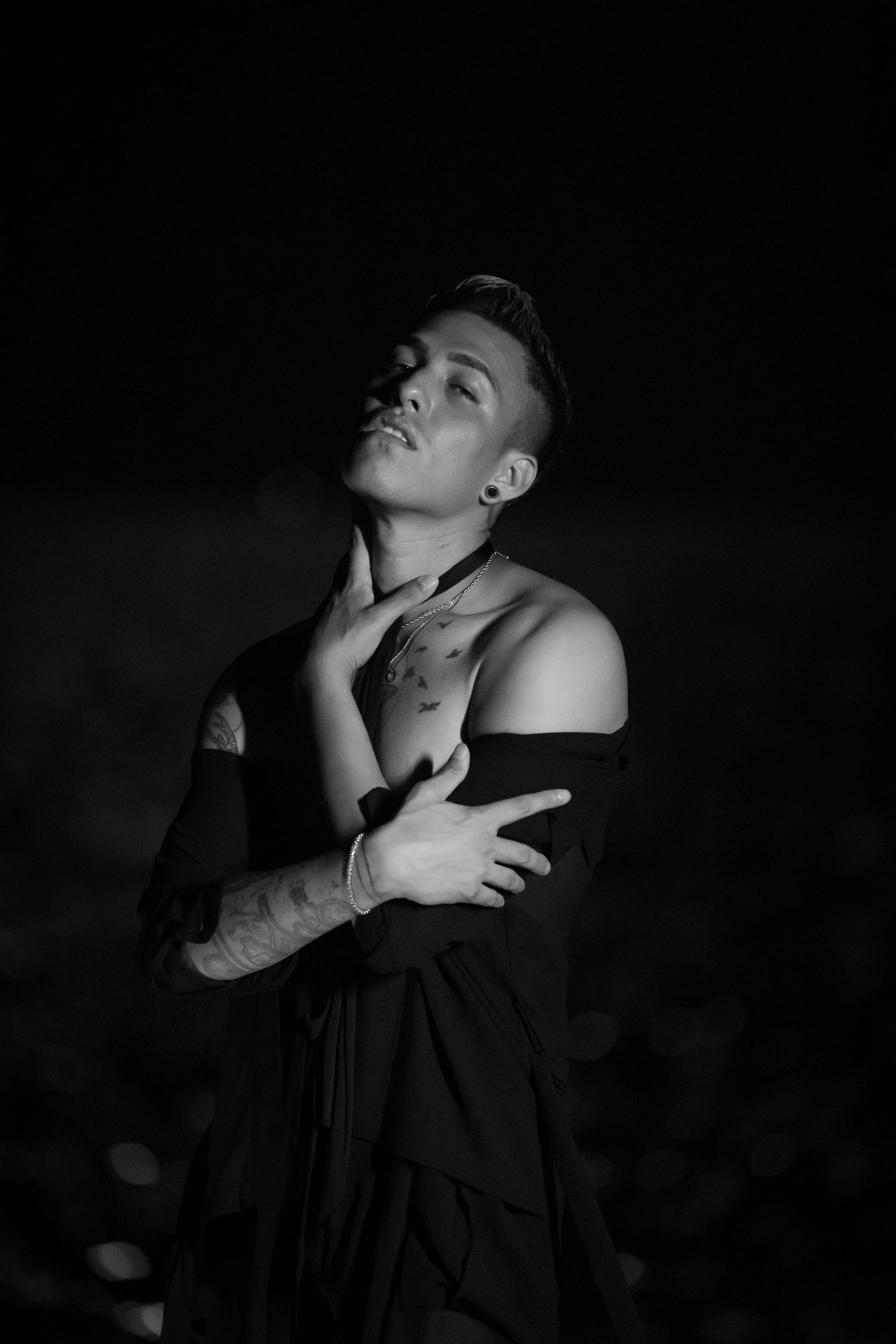 Black and white dramatic portrait with hands posed against dark background.