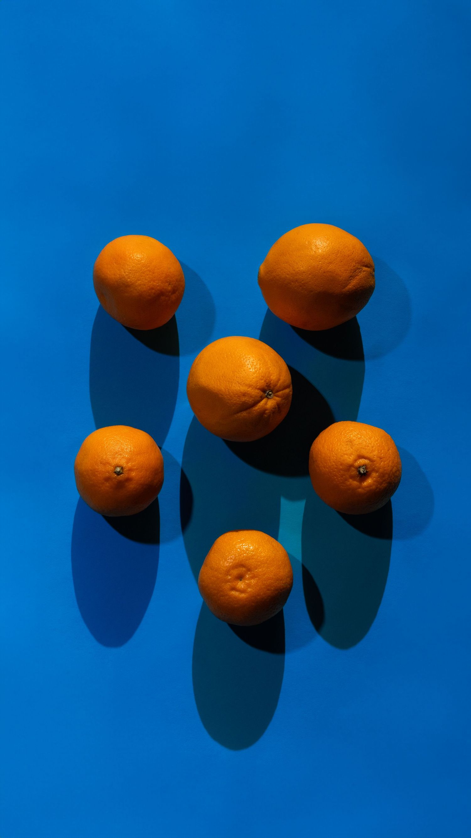 Fresh oranges casting dramatic shadows against a vibrant blue background in a minimalist food photography composition.