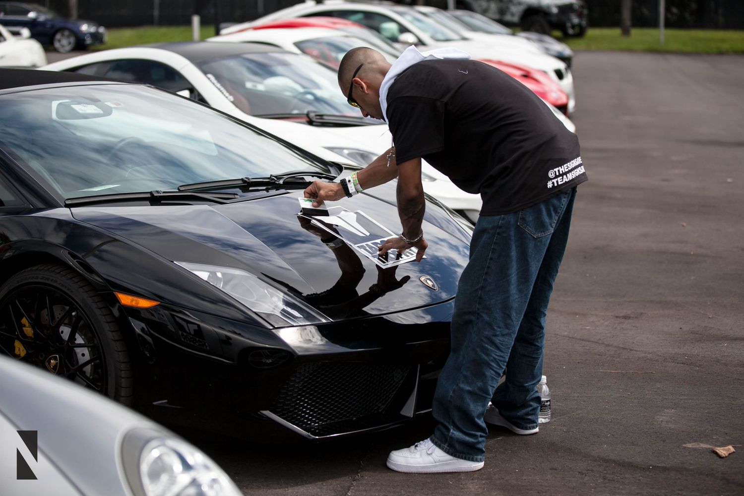Someone inspecting the hood of a black Lamborghini Murcielago in a parking lot.