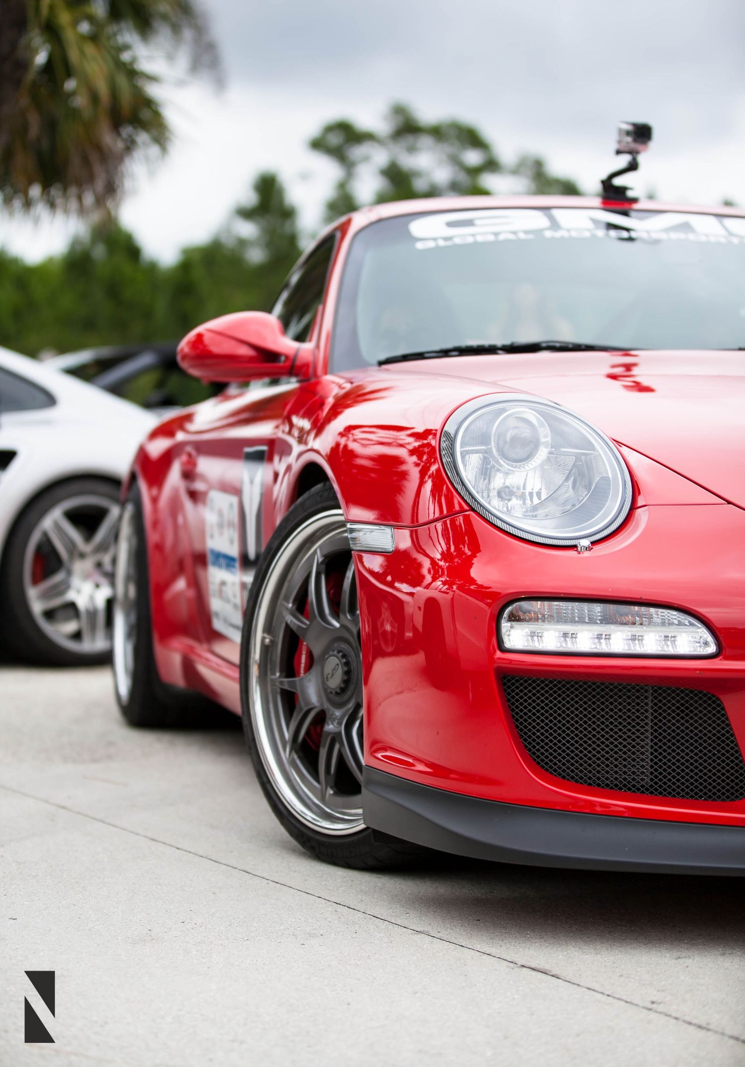 A bright red Porsche GT3 sports car with racing modifications and a mounted GoPro camera shown in profile view.