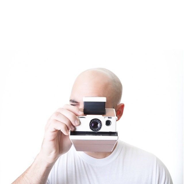 Minimal portrait of photographer holding vintage Polaroid camera against white background.