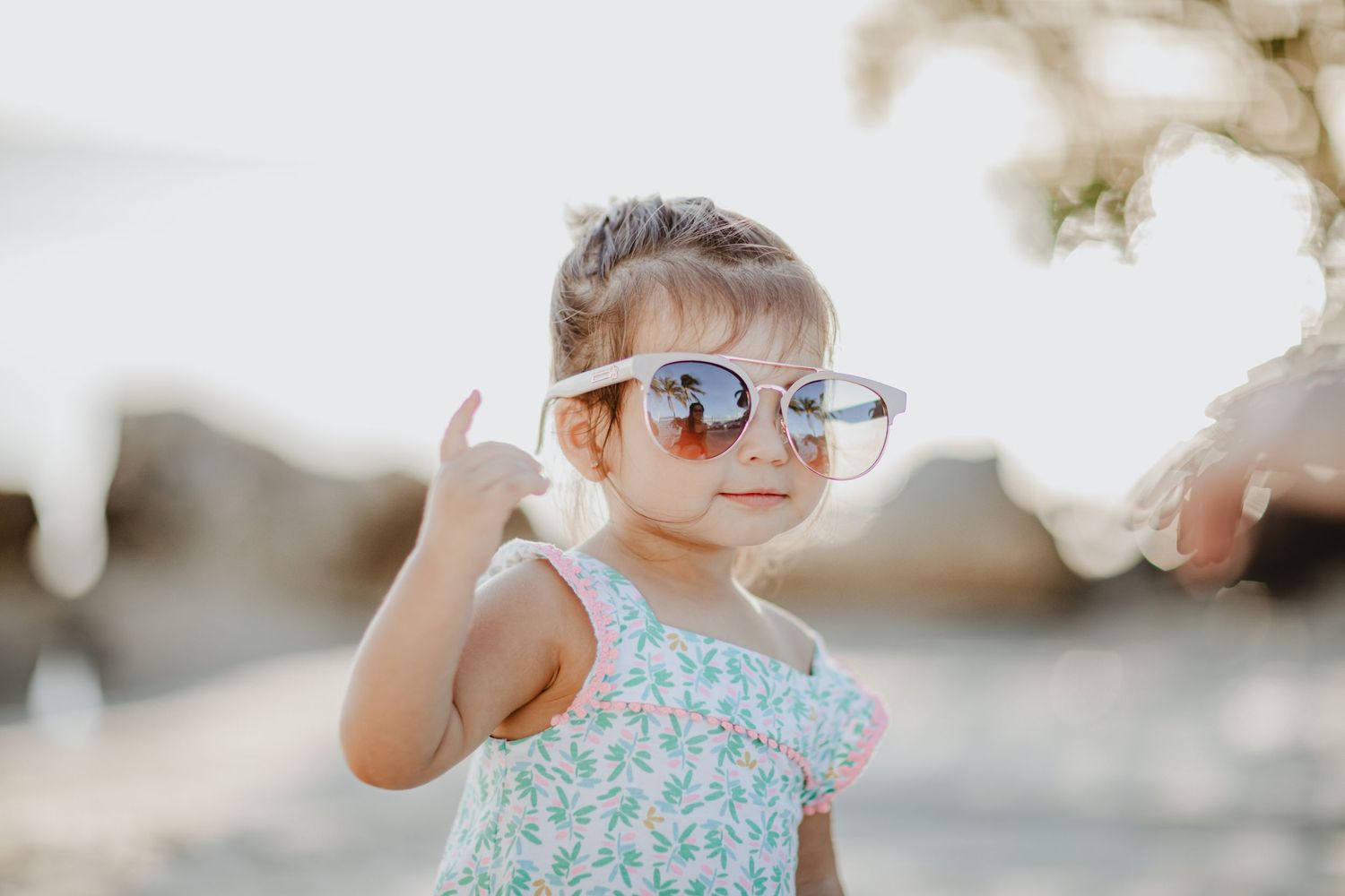 A child wearing sunglasses poses cheerfully on a sunny beach.