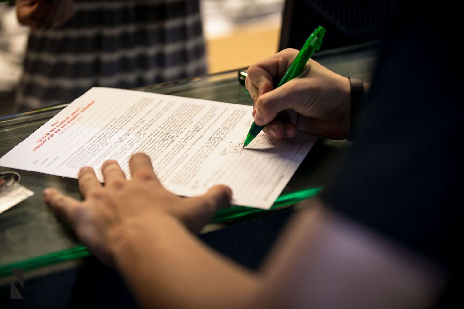 Close up view of hands filling out paperwork with a green pen on a dark surface.