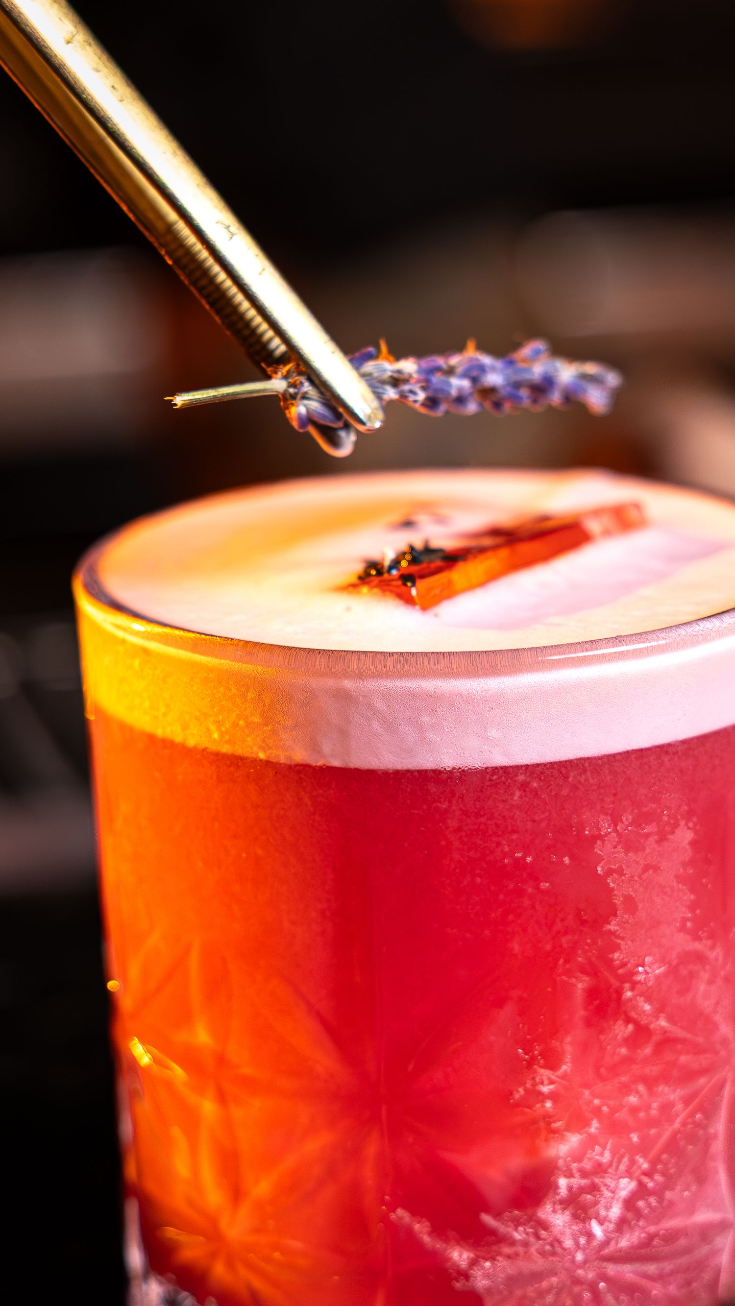 Closeup sequence of colorful cocktail drops being added to a vibrant red drink in a frosted glass.