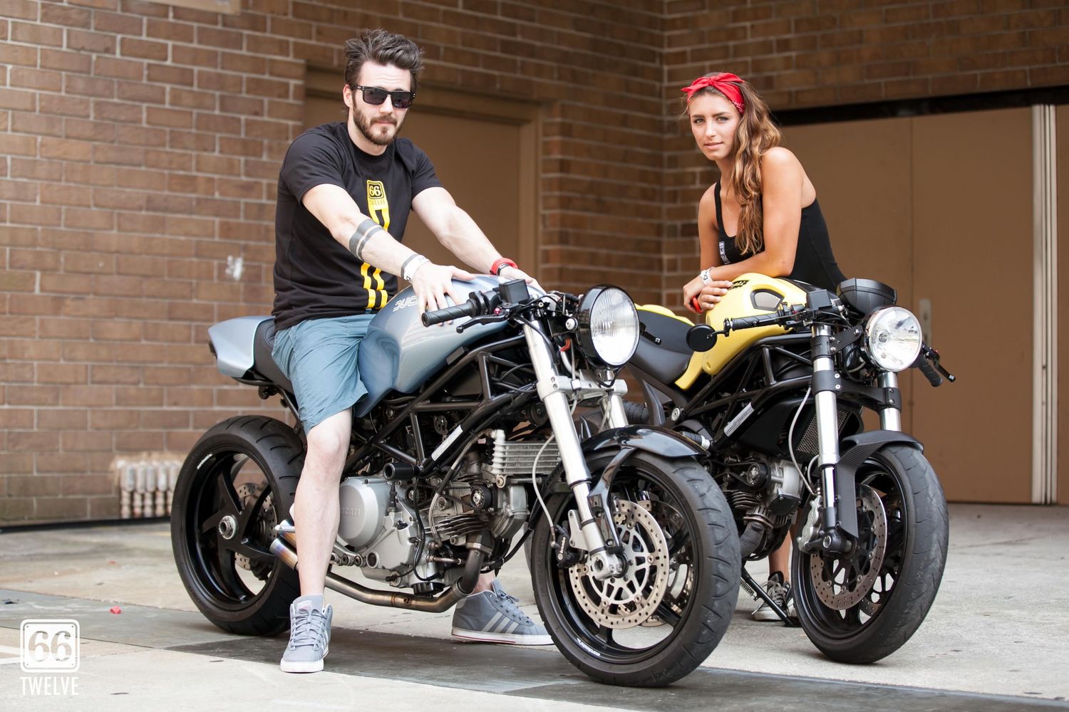 Two motorcyclists with their customized black sport bikes positioned in front of a brick wall.
