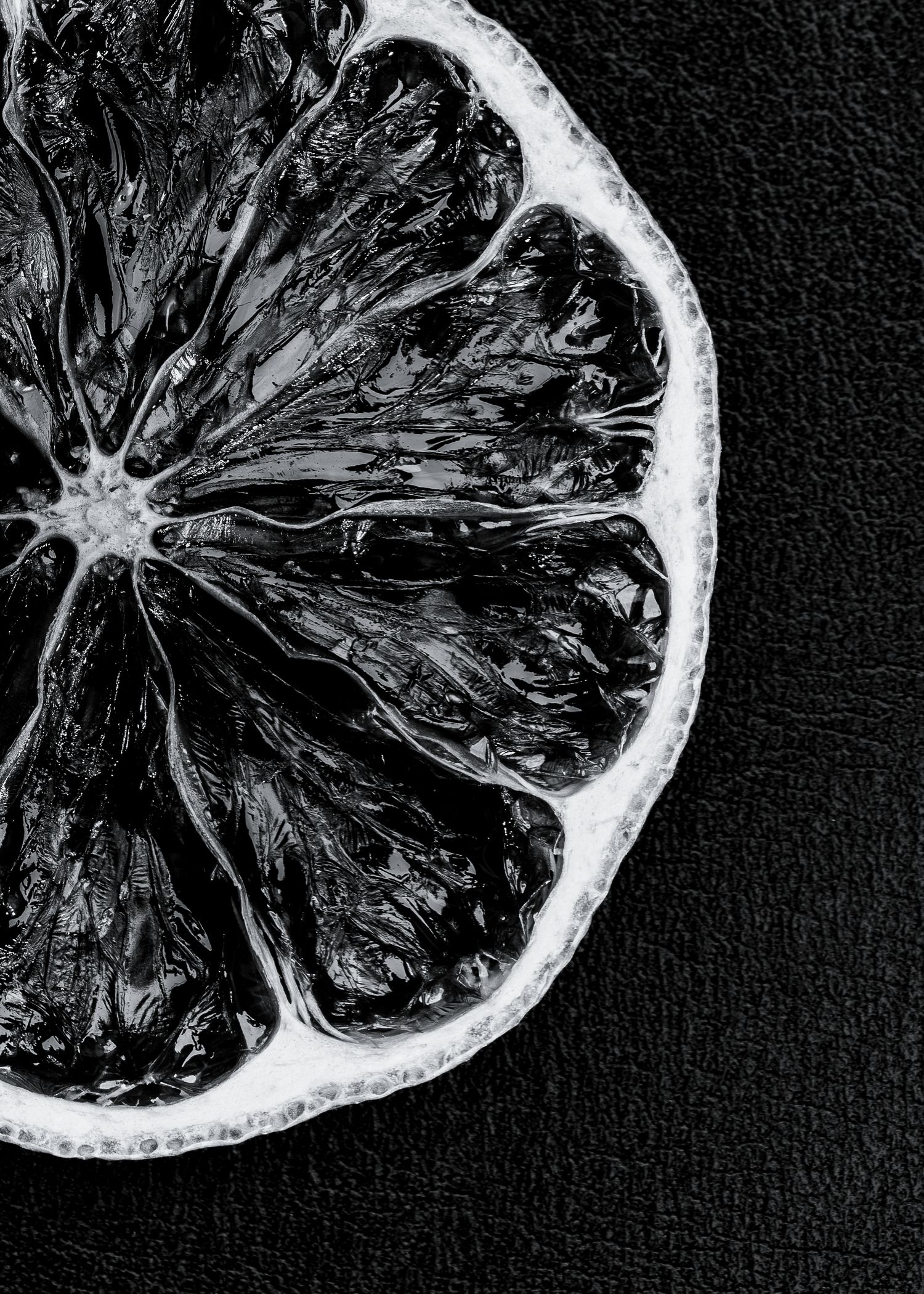 Black and white macro photograph of a sliced citrus fruit segment showing detailed pulp texture against dark background.