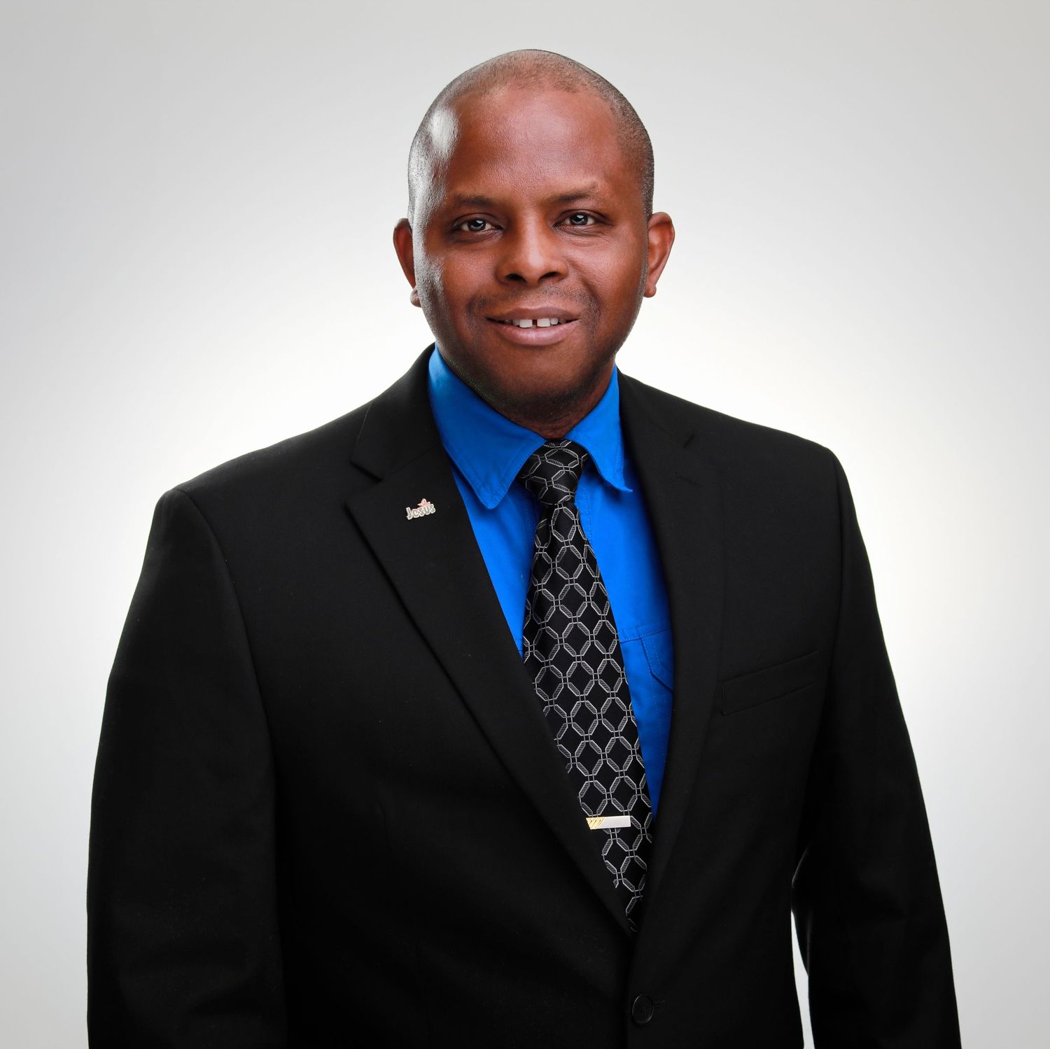 Professional portrait of person in black suit jacket and blue dress shirt with polka dot tie.