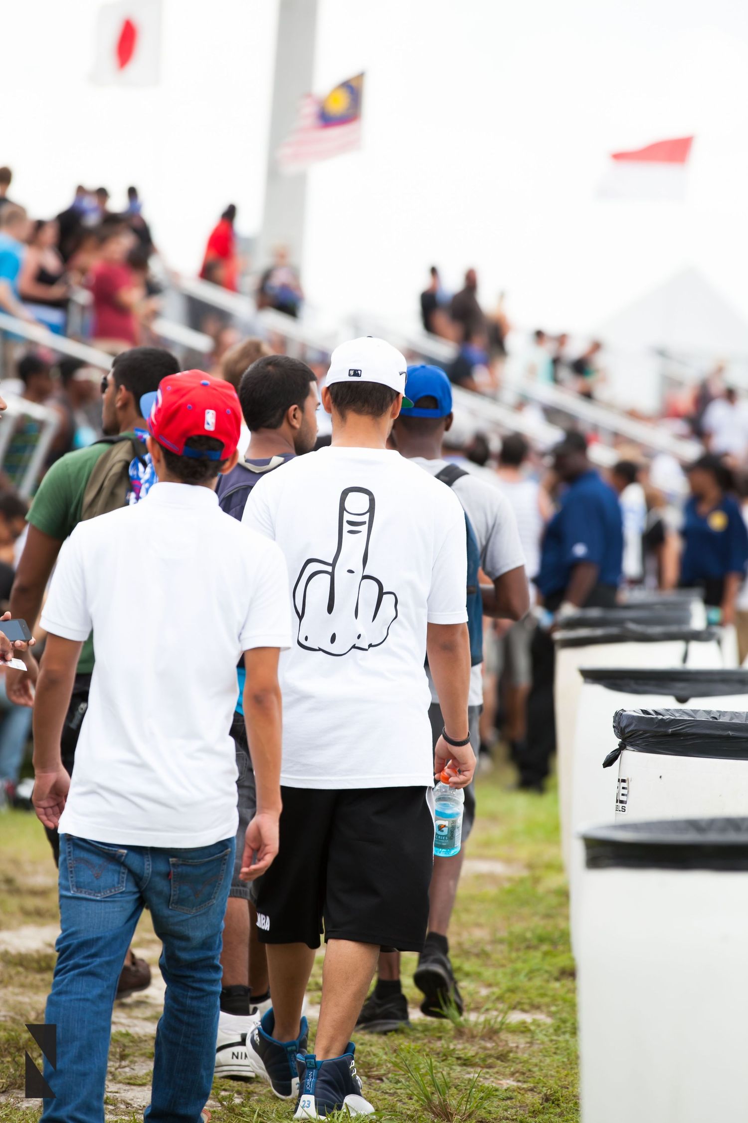 People walking at an outdoor event with one person wearing a t-shirt displaying a provocative hand gesture.