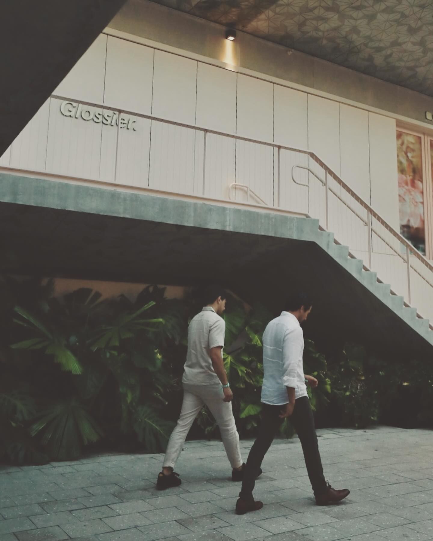 Two people walking under modern white architectural structure with stairs.