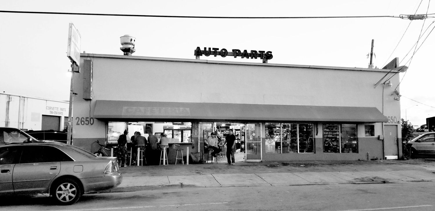 Black and white storefront of Auto-Parts shop with parked cars out front.