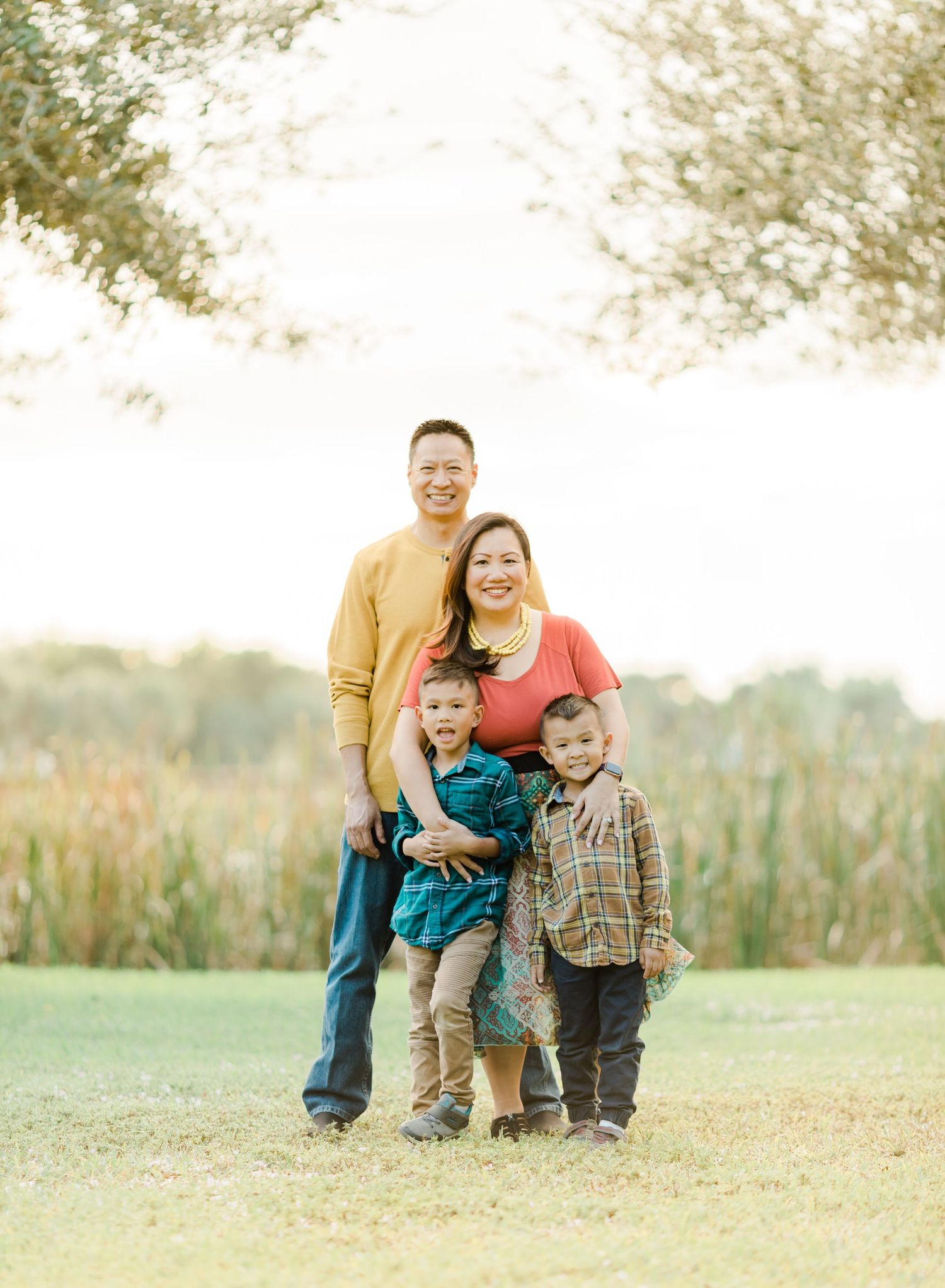 A family of four poses together outdoors in a grassy field at sunset.