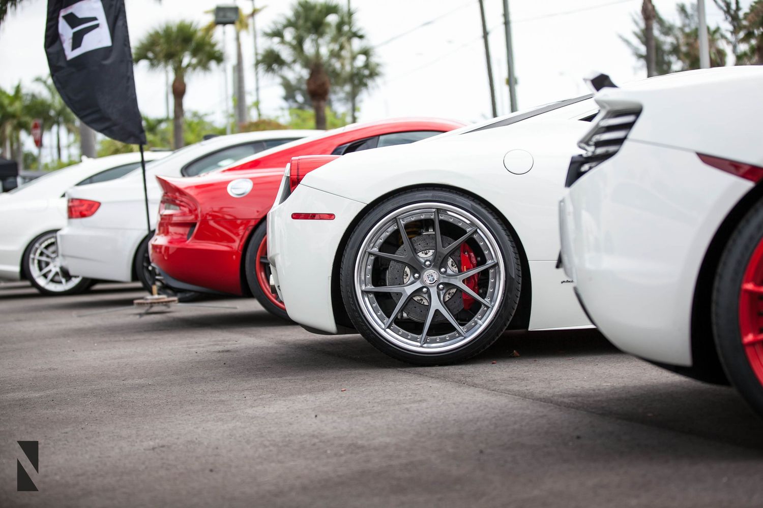 Close-up view of luxury sports car wheels and side panels in white and red at a car show event.