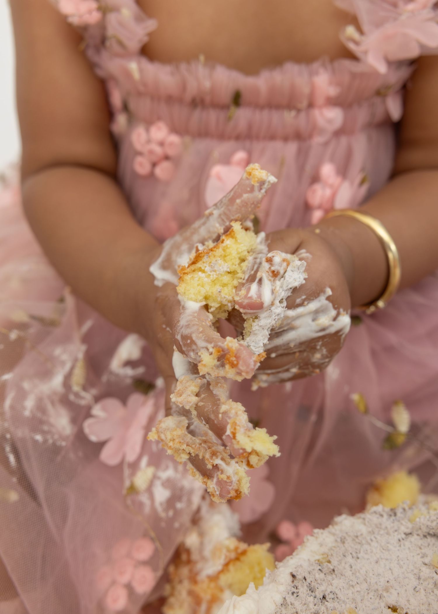 A person in a pink floral dress holds a partially eaten and crumbled slice of cake with frosting.
