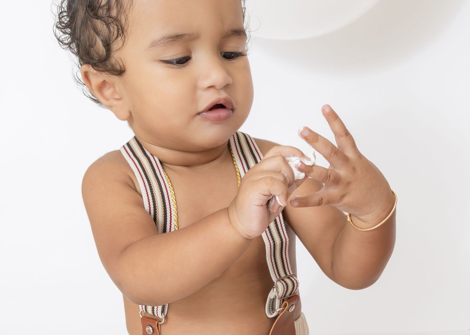 A baby in a white and brown striped romper plays and gestures during a studio photoshoot session.
