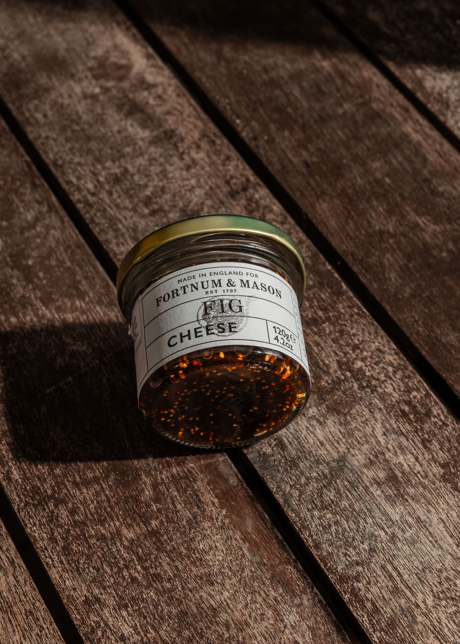 A jar of fig cheese sits on weathered wooden planks in dramatic lighting.