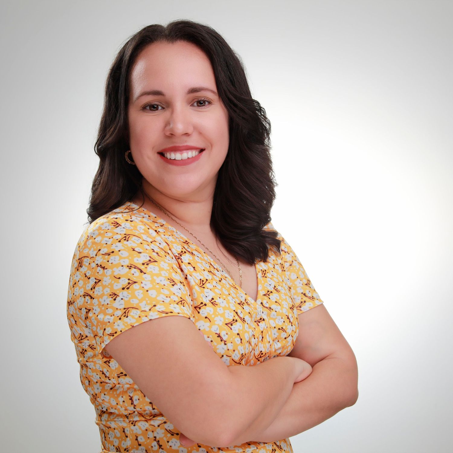 Professional headshot against a light background wearing a yellow floral print top with crossed arms.