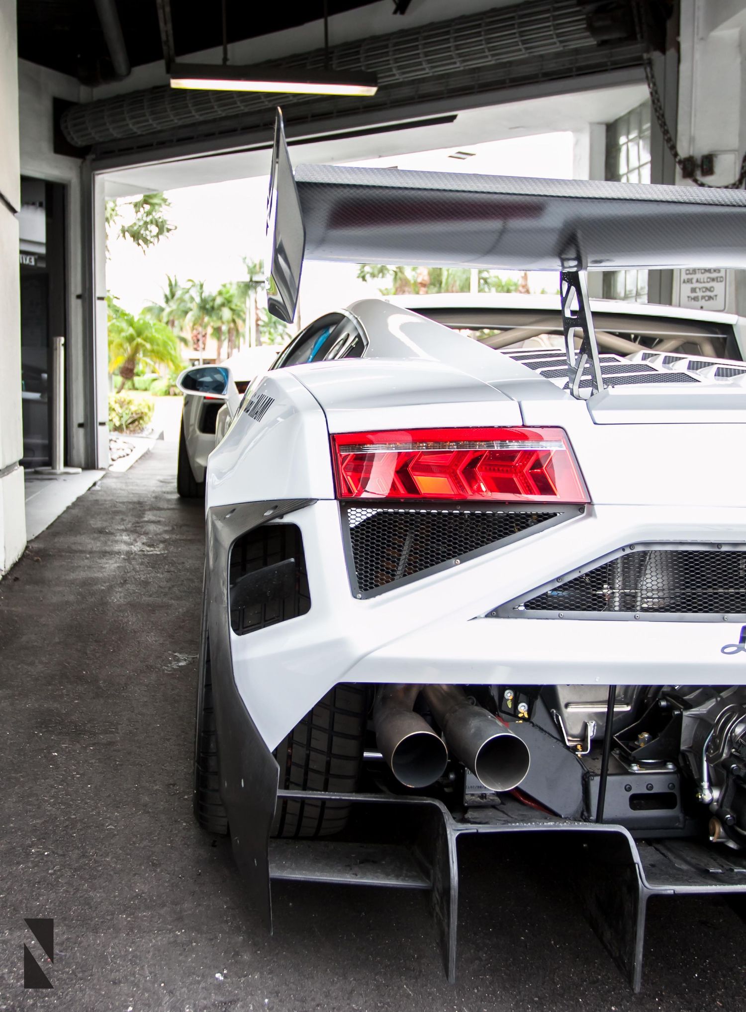 Rear view of a white Lamborghini supercar showing its dramatic taillights and dual exhaust system in a garage setting.