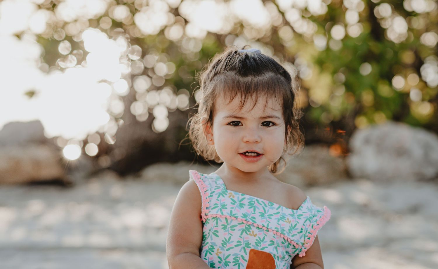 A child in a blue floral dress smiles while playing on a beach.