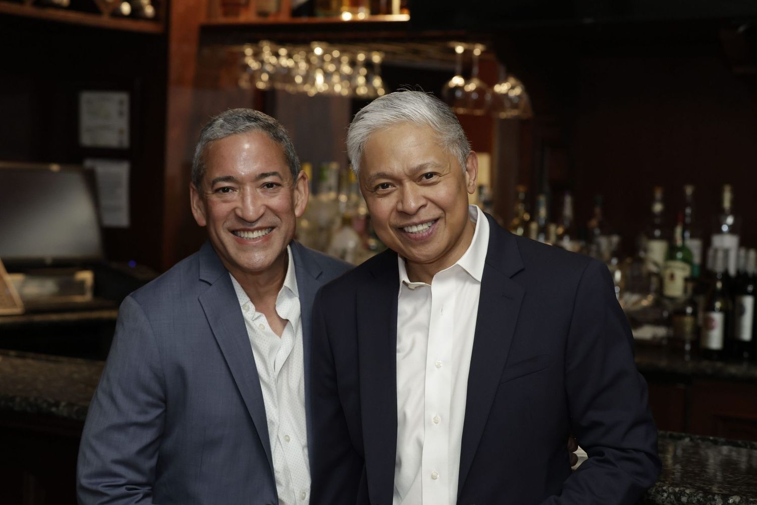 Two men in suits pose for photos at what appears to be a formal business or social gathering.