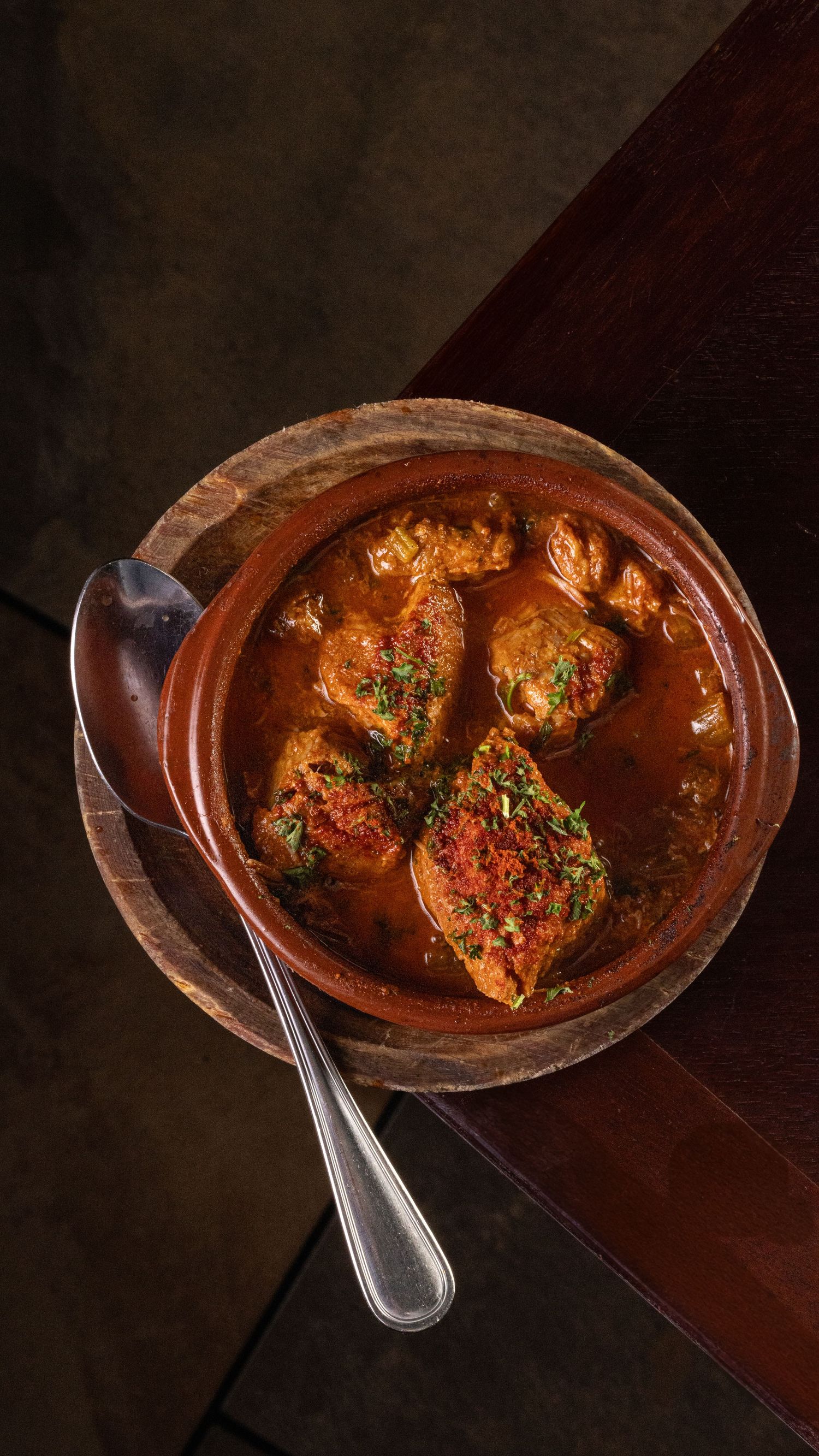 Traditional spicy curry with tender meat pieces swimming in a rich red gravy served in a rustic clay bowl.